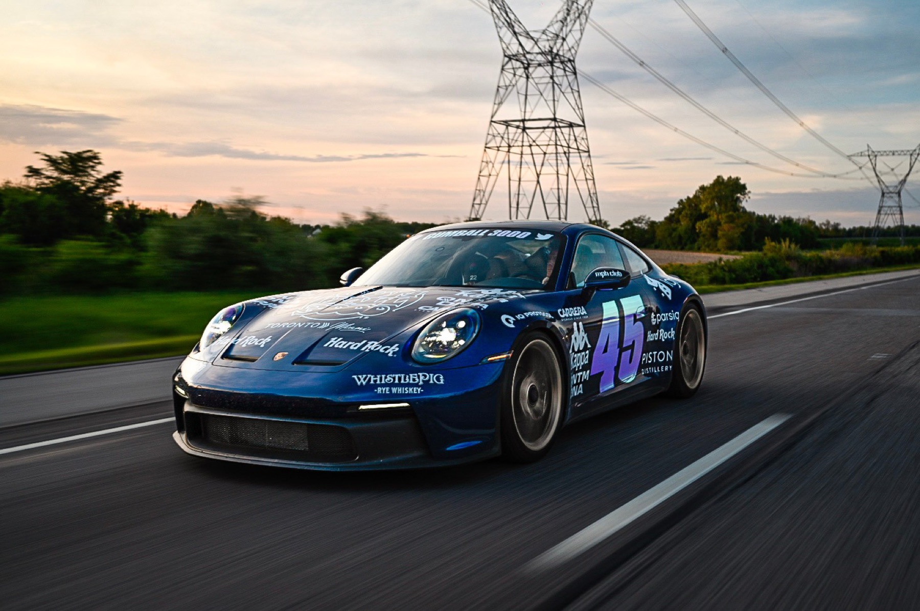 Porsche 911 GT3 in Gumball 3000 livery rolling at sunset